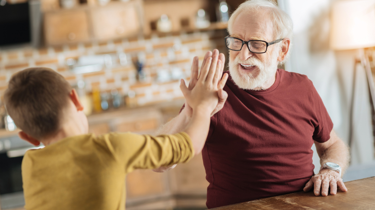 Perfect team. Positive delighted joyful grandfather and grandson smiling and being in a positive mood while giving each other high five.