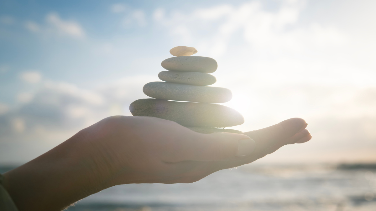 Finding Balance: How To Simplify Your Finances Without Losing Joy 1 Concept of harmony, positive mind, mental health. Balance of stones on a human hand, close-up against the sea and sun. Enjoying life, balancing body, mind, soul and spirit.
