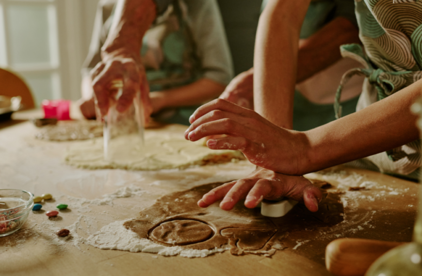 Close-up of family baking cookies together, hands busy with rolling and cutting dough on a kitchen counter, showing teamwork, joy, and love in the process of cooking for save money on holiday meals.