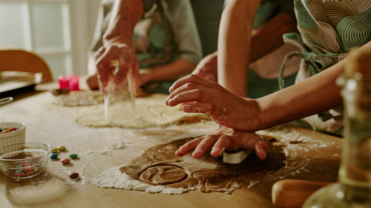 Close-up of family baking cookies together, hands busy with rolling and cutting dough on a kitchen counter, showing teamwork, joy, and love in the process of cooking for save money on holiday meals.