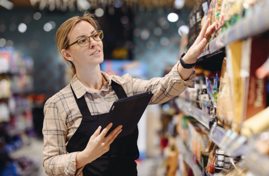 Young seller woman wearing uniform hold digital tablet pc computer check aisle arrange for shopping at supermaket store grocery shop buying choose products inside hypermarket. Purchasing food concept.