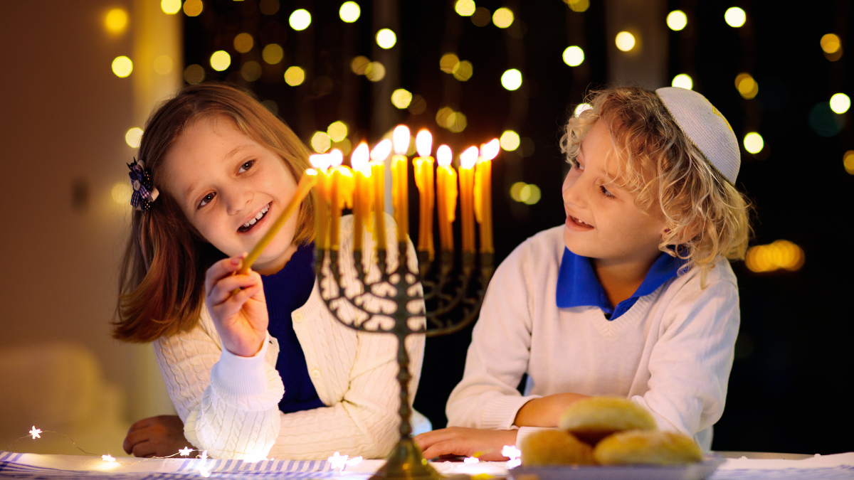 10 Frugal Hanukkah Traditions To Start With Your Family 1 Kids celebrating Hanukkah. Jewish festival of lights. Children lighting candles on traditional menorah. Boy in kippah with dreidel and Sufganiyah doughnut doing frugal Hanukkah tradition.