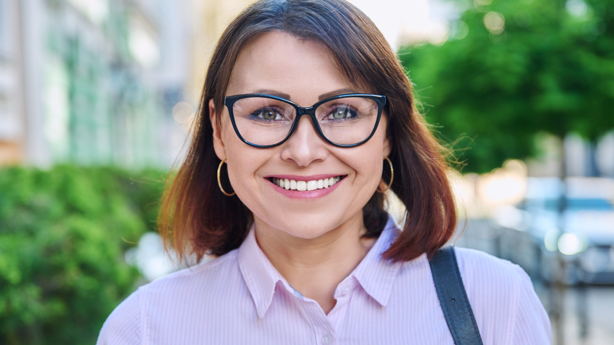 Headshot of smiling middle aged woman looking at camera outdoor.