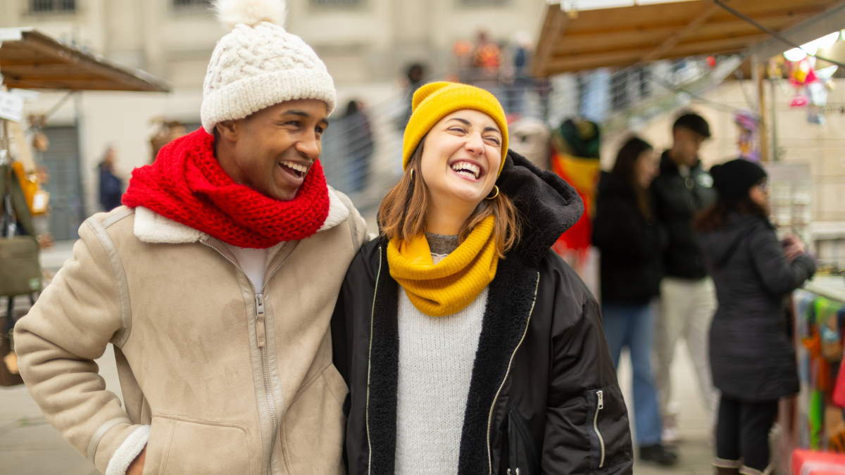 Happy multi ethnic couple is laughing and walking together visiting a christmas market during winter holidays.