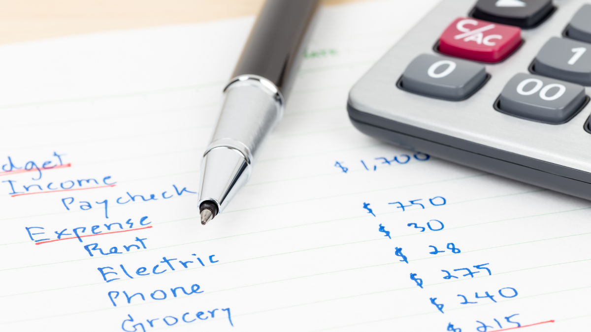 Hand writing home budget with calculator to show how to set up a monthly budget.