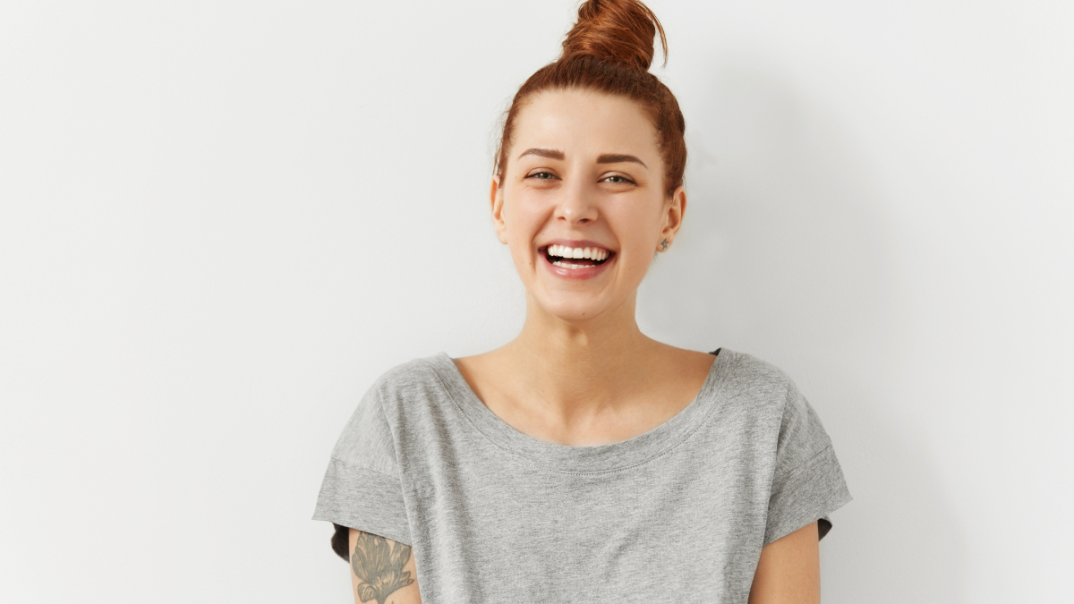 Happy cheerful young woman wearing her red hair in bun rejoicing at positive news or birthday gift, looking at camera with joyful and charming smile. Ginger student girl relaxing indoors after college.