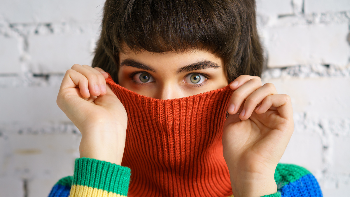 Portrait of a young woman in a multicolored sweater, covering her face with a sweater . The concept of shyness. 7 Frugal Moves Are a Waste of Time.