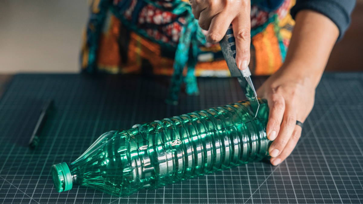 Close-up of hands using cutter on plastic bottle, promoting environmental awareness through reuse and upcycling.