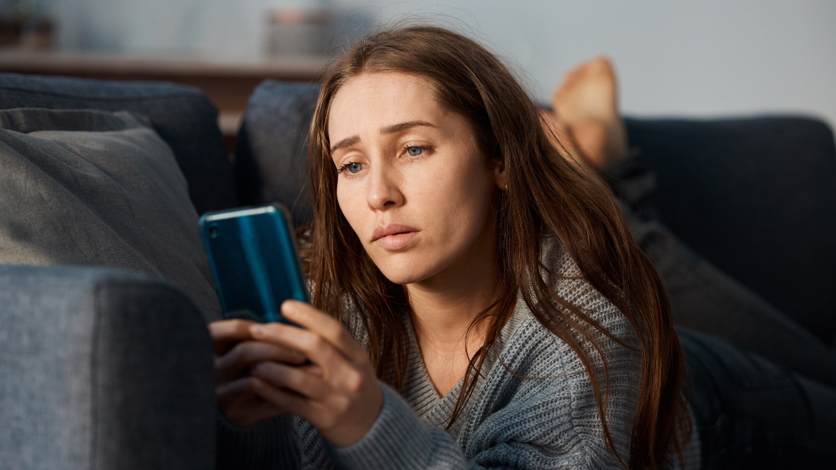 Depression, lonely or sad woman on sofa with phone for social media addiction or stress in home. Heartbroken, fear or person reading online story or cyberbullying message on mobile app with anxiety.