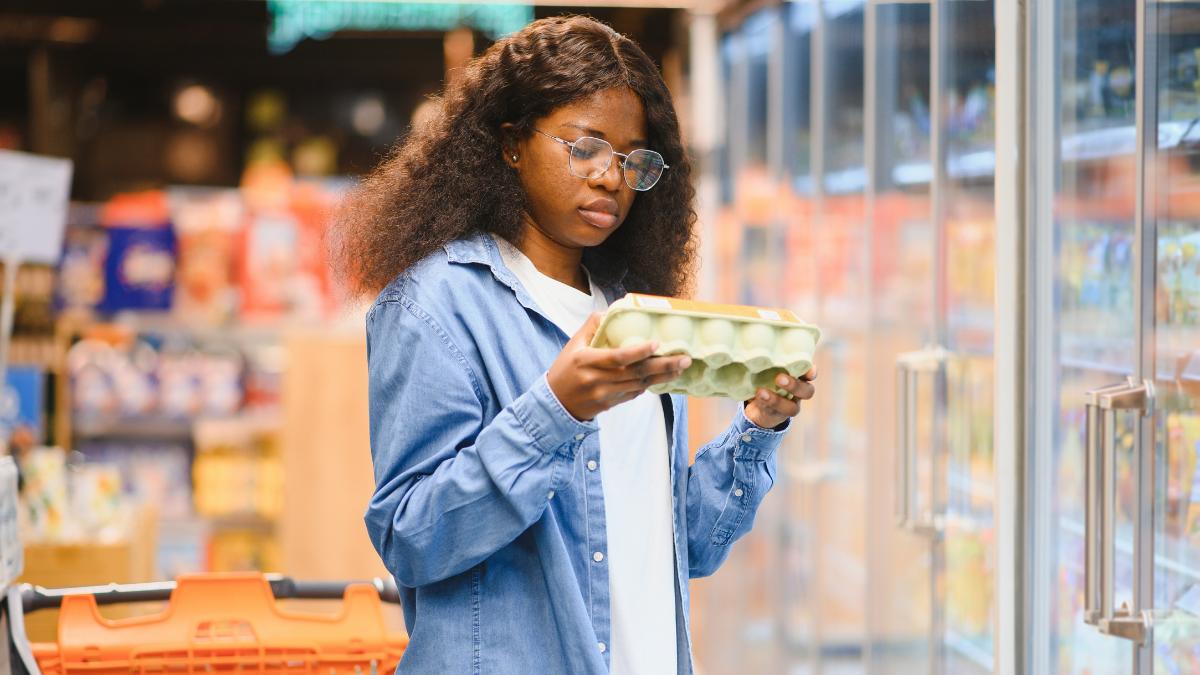 Smiling curly hair African American woman In supermarket checking boxes with fresh eggs.