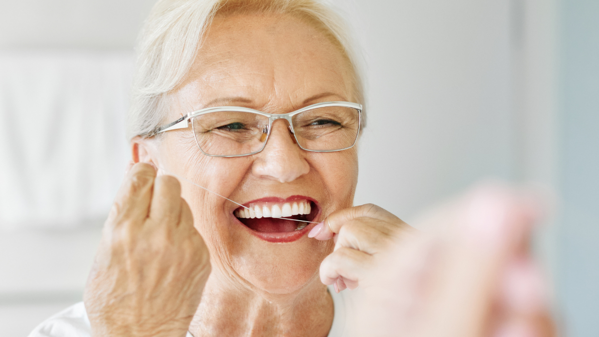 Portrait of an elderly senior woman is cleaning brushing his teeth using dental floss in front of mirror in bathroom. Dental hygiene, vitality and beauty concepts.