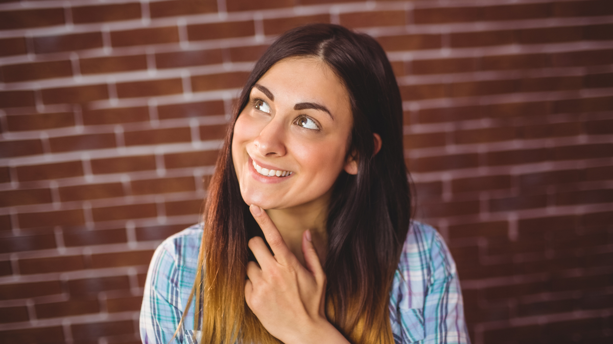 Pretty hipster smiling and thinking on red brick background.