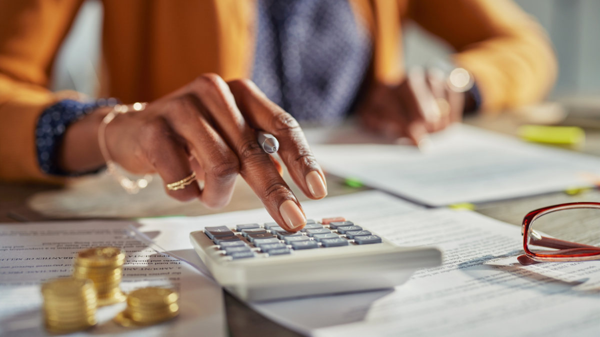 Close up of african american woman hands calculating tax while working at desk. Casual businesswoman using calculator to check monthly income and expenses of her freelance activity.