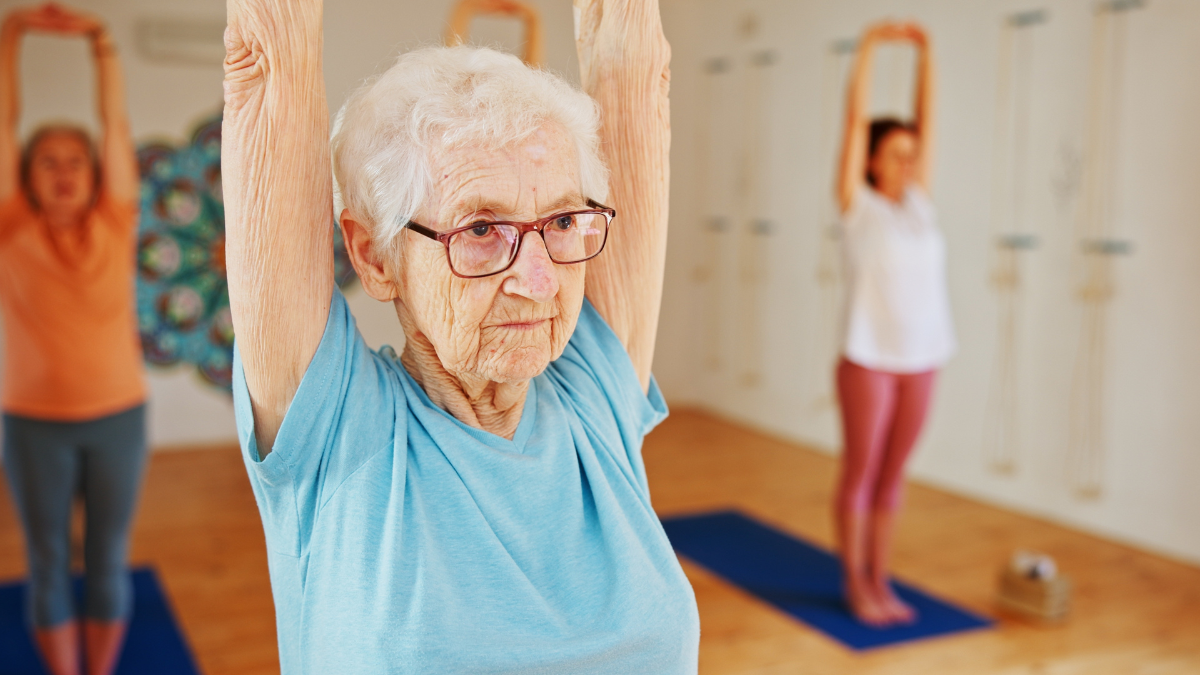 Senior woman, yoga or stretching with class for holistic health, mindfulness or wellness. Elderly, female person or yogi with arms up in pilates for spiritual workout, exercise or fitness in studio.