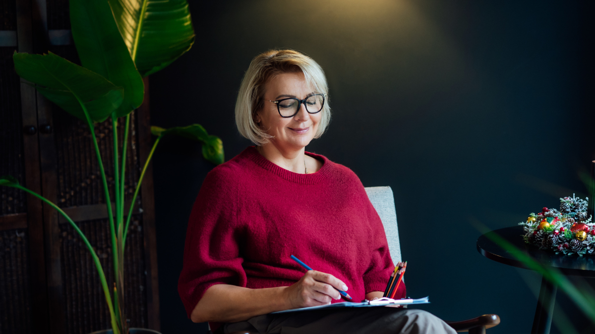Woman drawing work-life balance wheel sitting on armchair at cozy dark home interior. Self-reflection, life planning for next new year. Personal Year review. Coaching tools. Finding Balance in Life.