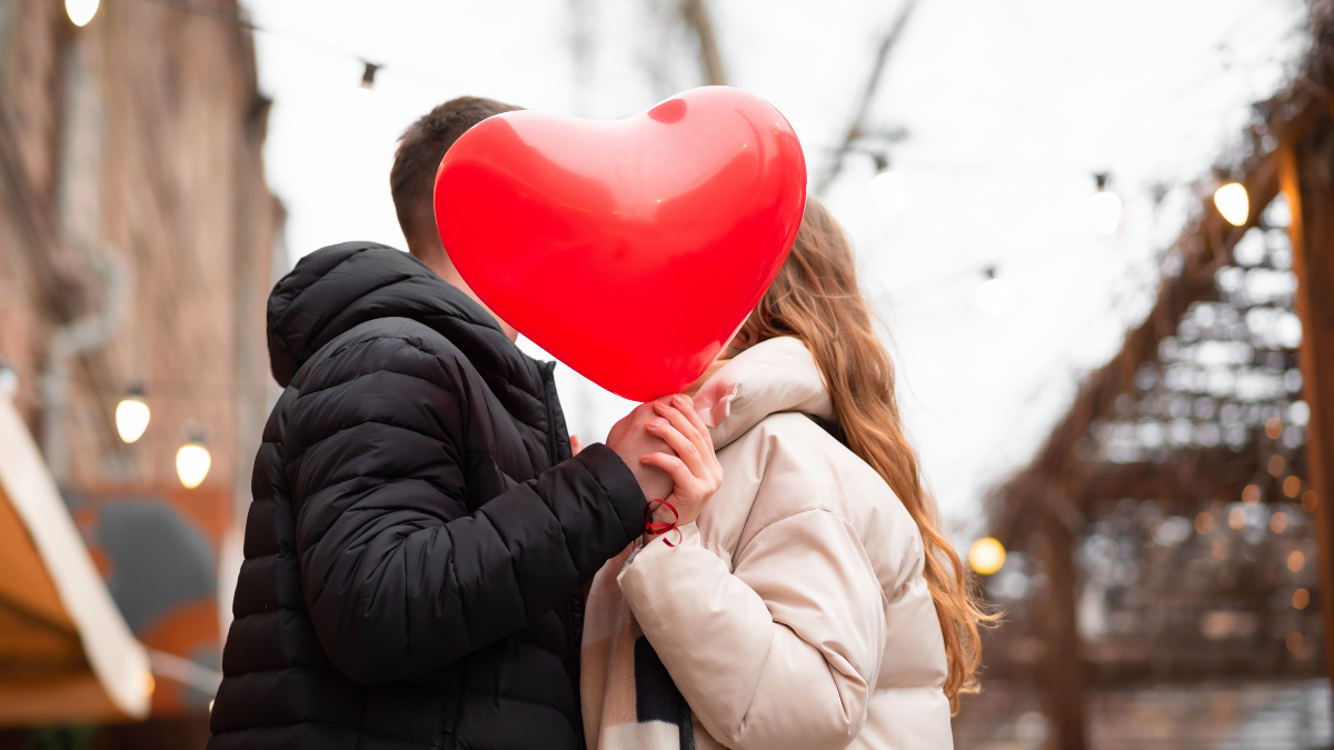 Couple holding a heart-shaped balloon and kissing on the street. Valentine's day concept, gifts, love. Low Budget Valentines Day Ideas.