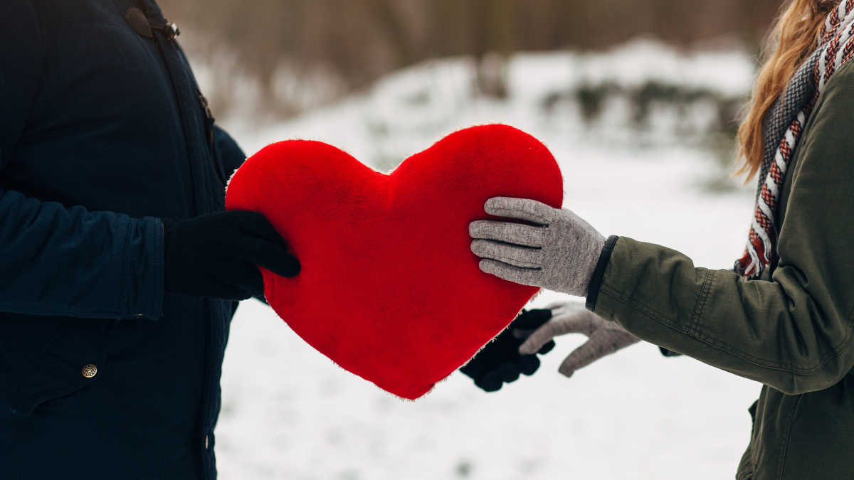 Young couple man and woman holding red big heart in hands in winter Park.