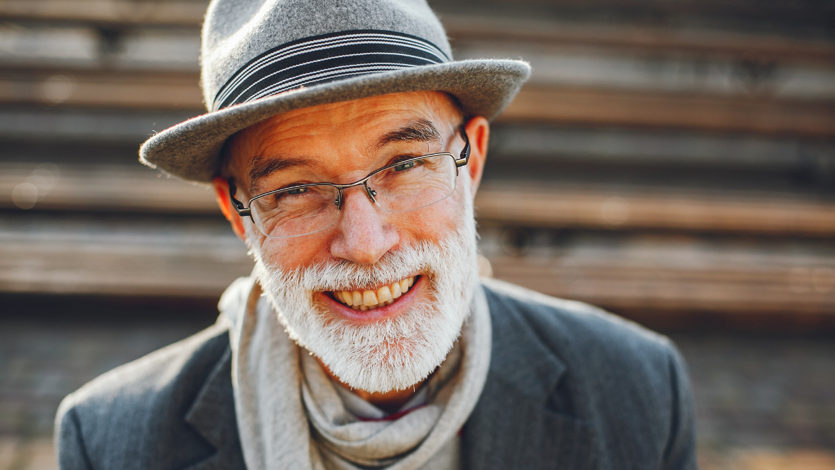 Handsome grandfather in a autumn park. Old man in a gray jacket and hat. Male sitting on the bench.