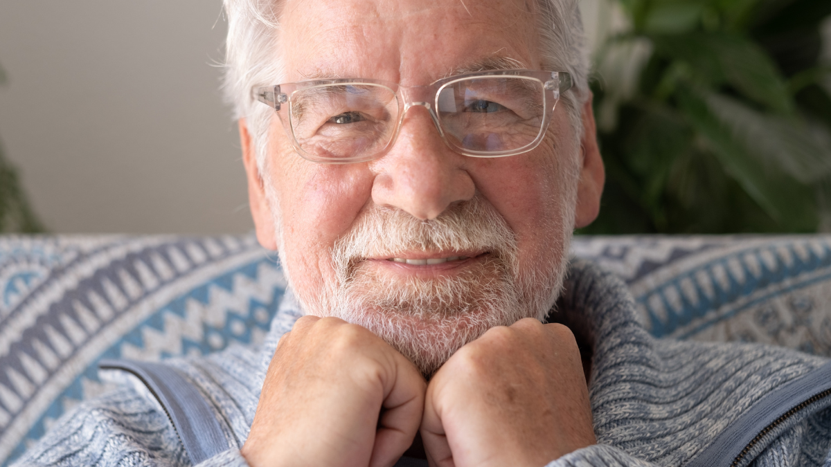Portrait of serene bearded senior man relaxing on sofa at home looking at camera smiling. Headshot of elderly attractive man enjoying retirement.
