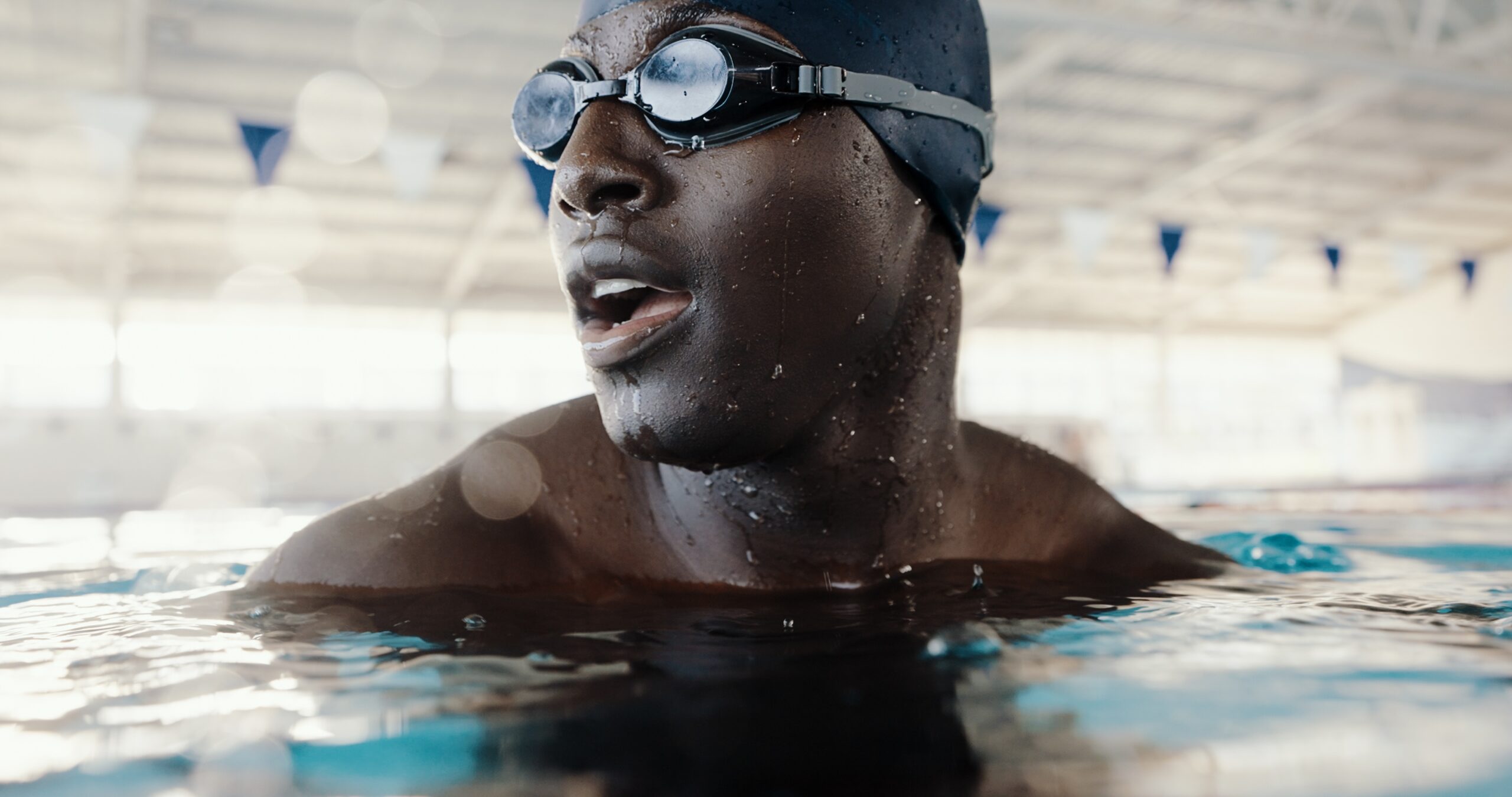 Swimming, workout and man in pool, water and practice for competition, healthy or routine in morning. Swimmer, athlete and black person with goggles for performance, exercise or preparation for sport.