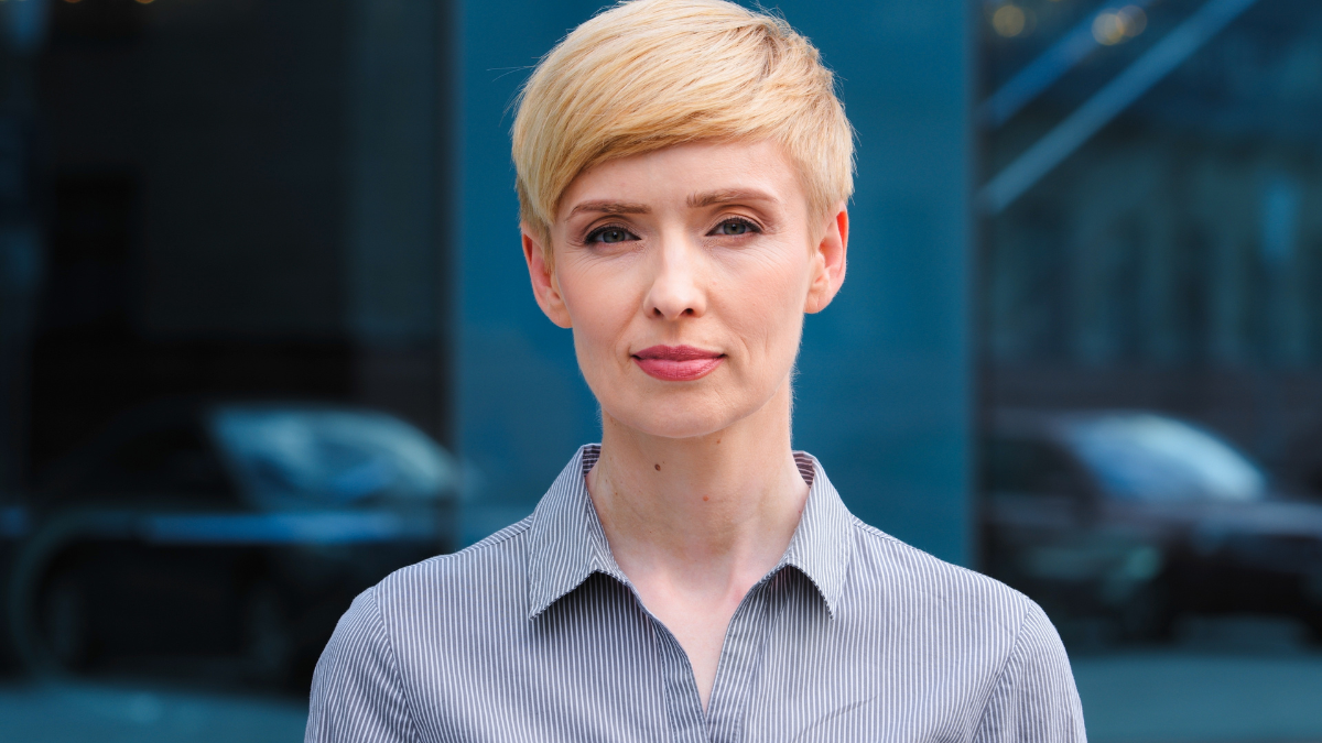 Close-up female serious face headshot portrait outdoors caucasian middle aged business woman boss blonde short haired lady wears formal shirt unhappy calm looking at camera standing posing on street.