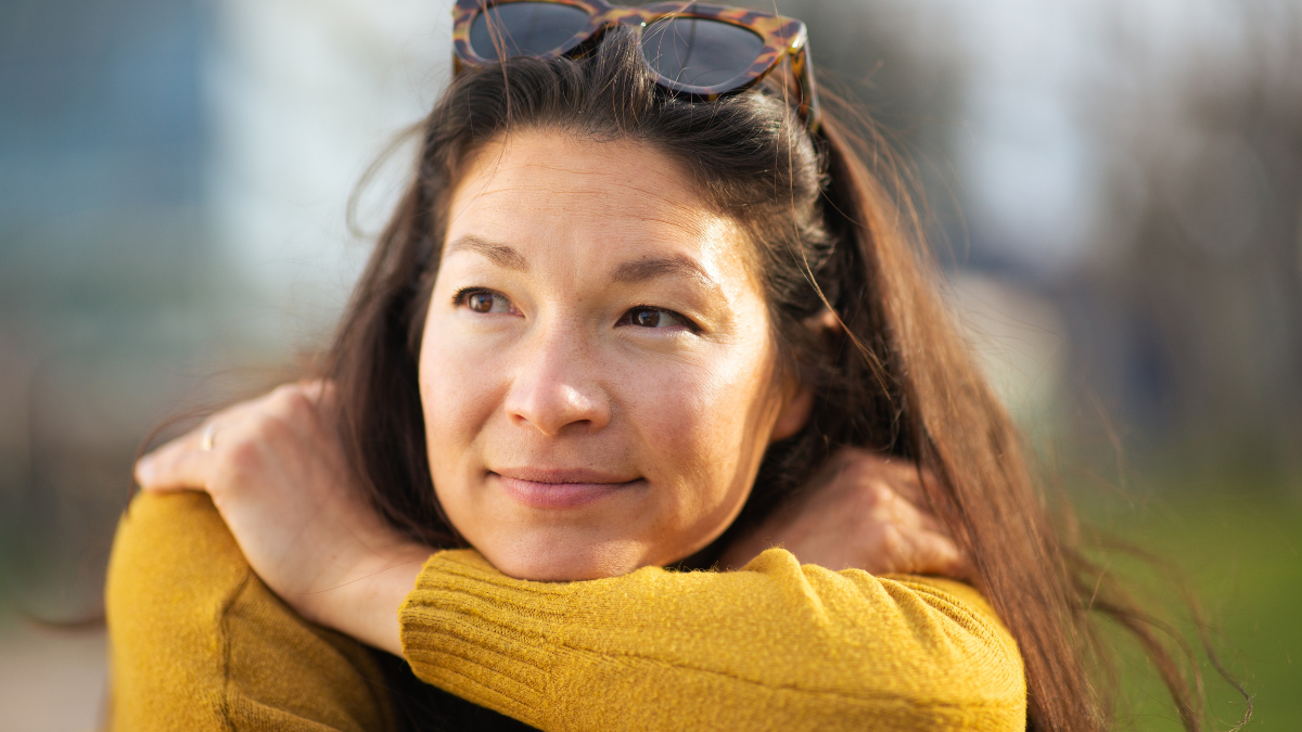 Close up portrait of beautiful asian woman sitting outside looking away and thinking.