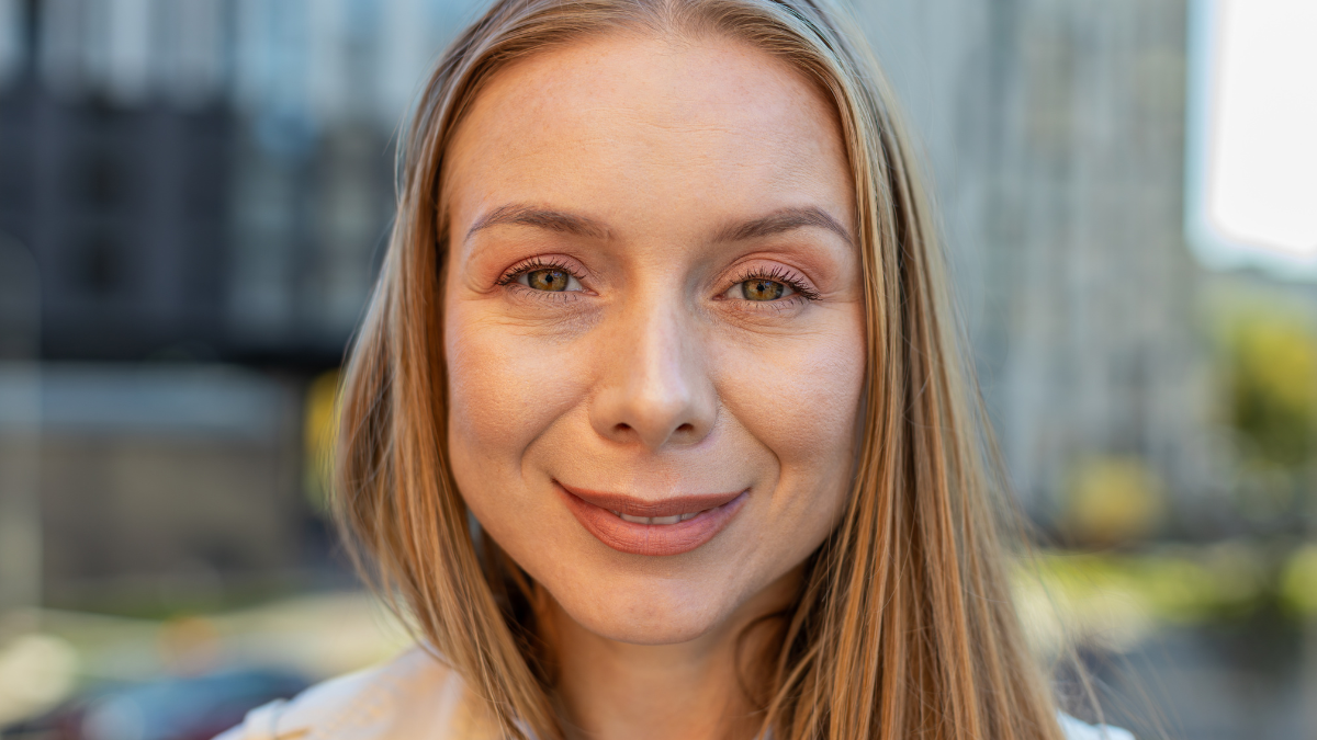 Close-up portrait of happy mature woman face smiling friendly looking at camera resting relaxation feel satisfied good news outdoors. Pretty adult lady with blond hair in coat on downtown city street.