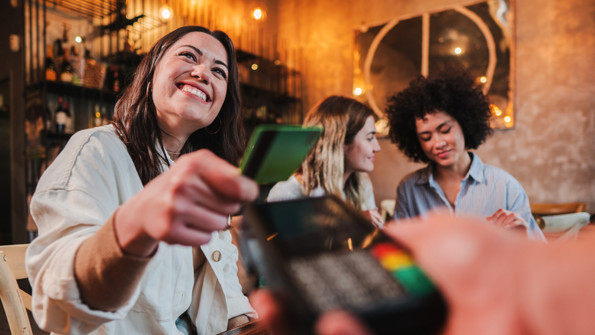 Happy young woman paying bill with a contactless credit card in a restaurant. Female smiling holding a creditcard and giving a payment transaction to the cashier. High quality photo Ways to Avoid Impulsive and Compulsive Spending.