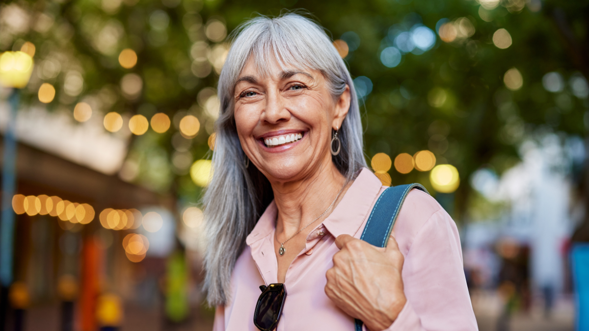 Close up face of happy retired senior woman in smart causal smiling. Elderly healthy lady in pink shirt with grey hair smiling on urban street. Confident mature woman looking at camera with a smile ways to be more frugal.