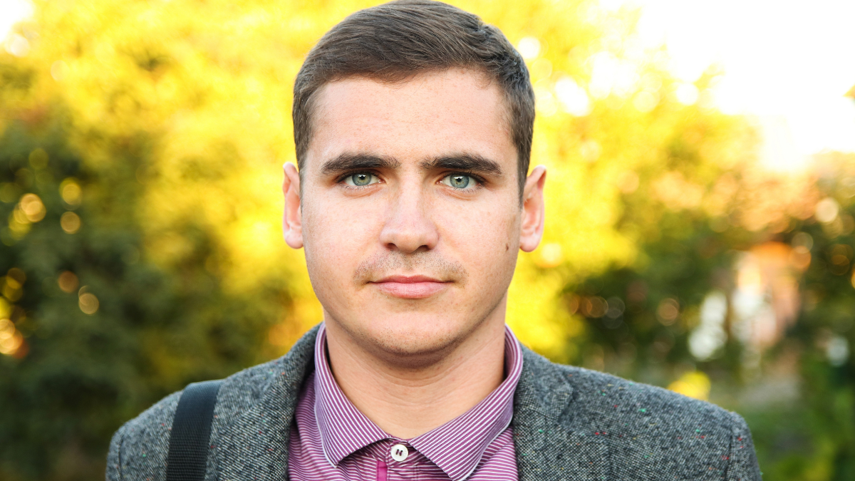 Millennial man, 20-29 years old, walking in nature during autumn, close-up portrait. Blurred summer background, close-up portrait of a Caucasian male in his 20s, autumn setting.