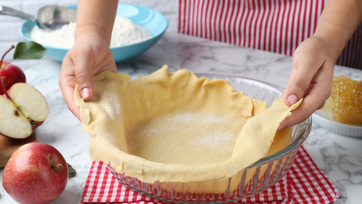 Woman putting dough for apple pie into baking dish at white marble table, closeup new hobby.