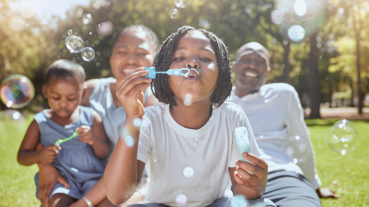 Happy, nature and black family blowing bubbles while playing, bonding and enjoying summer in the park. Happiness, father and mother with children having fun together in a green garden Things To Do Outside as a Family.