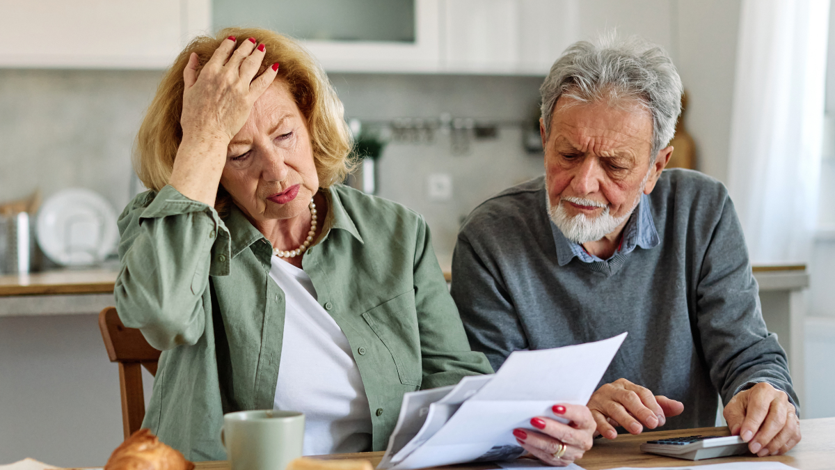 Senior couple checking bills and calculating expenses using a calculator at home, debt taxes and home budget concept, worried married elderly couple 5 signs your debt is out of control.