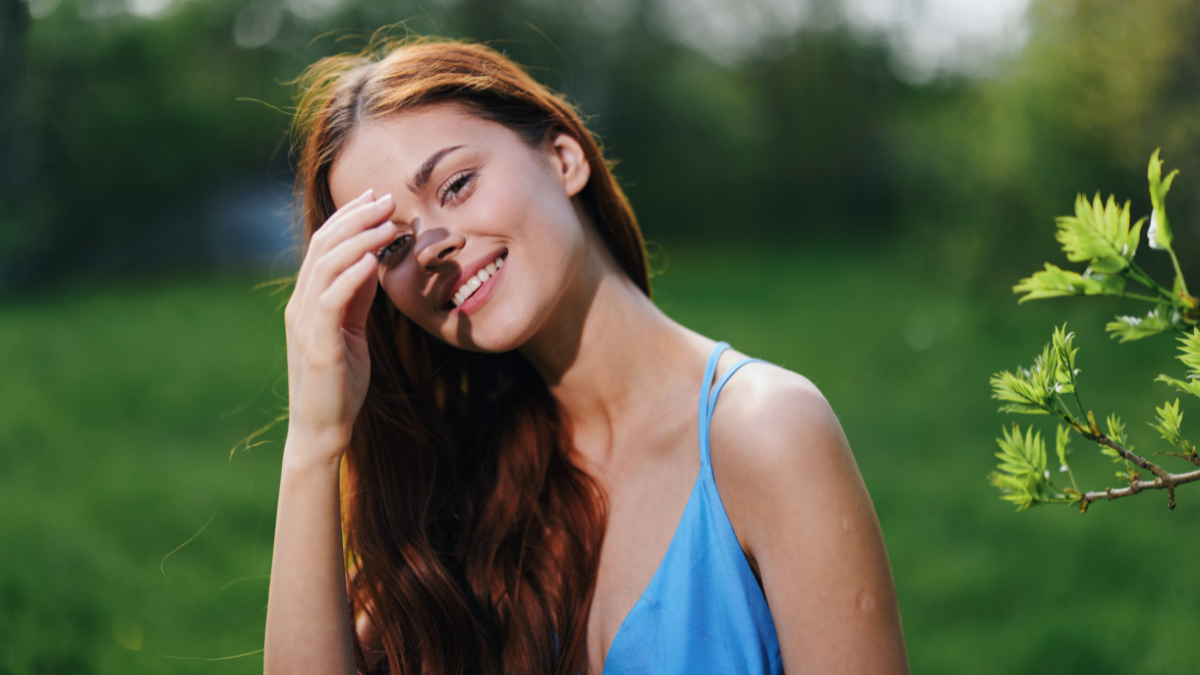 A woman in the spring nature smile with teeth touching hand long natural hair and happy, the concept of a healthy body and healthy hair in the spring and summer in the sun.