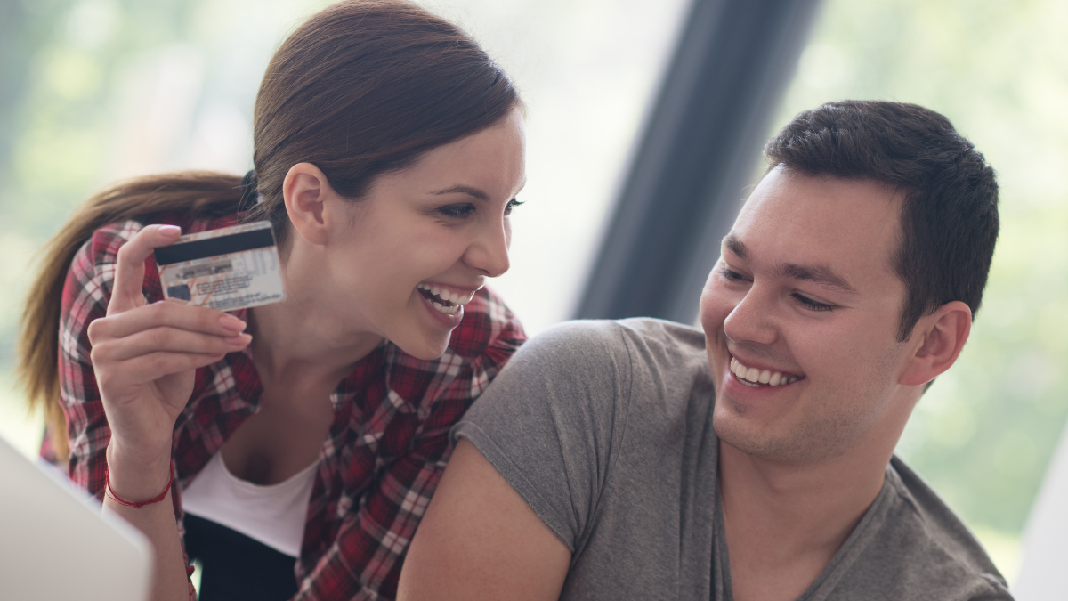 happy young couple buying online using laptop a computer and a credit card in their luxury home villa. Combining Finances With Your Spouse.
