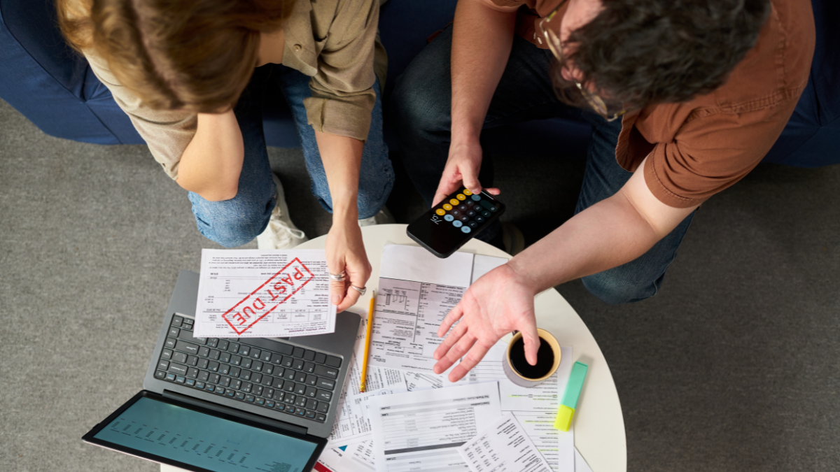 Caucasian young woman and Caucasian young man sitting at table reviewing tax documents with laptop and calculator, holding overdue bill marked past due, appearing stressed Debt Avalanche Method.