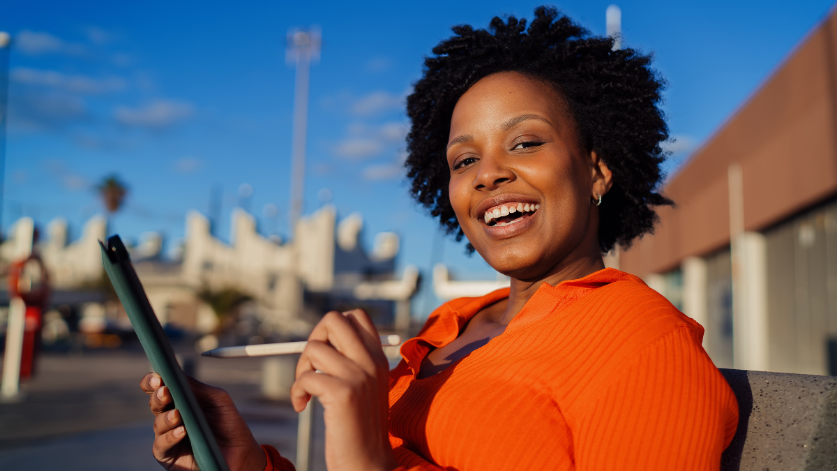 Smiling woman using digital tablet and stylus outdoors, happy female freelancer drawing or planning on tablet screen, successful career and creative digital nomad concept, sunshine.