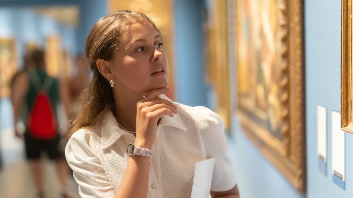 Museum female visitor with paper in hands walk through exhibition halls museum. Girl with guidebook inspects paintings of various artistic genres. Exposition, admires works of Renaissance artists How To Get Free Passes to Zoos and Museums.