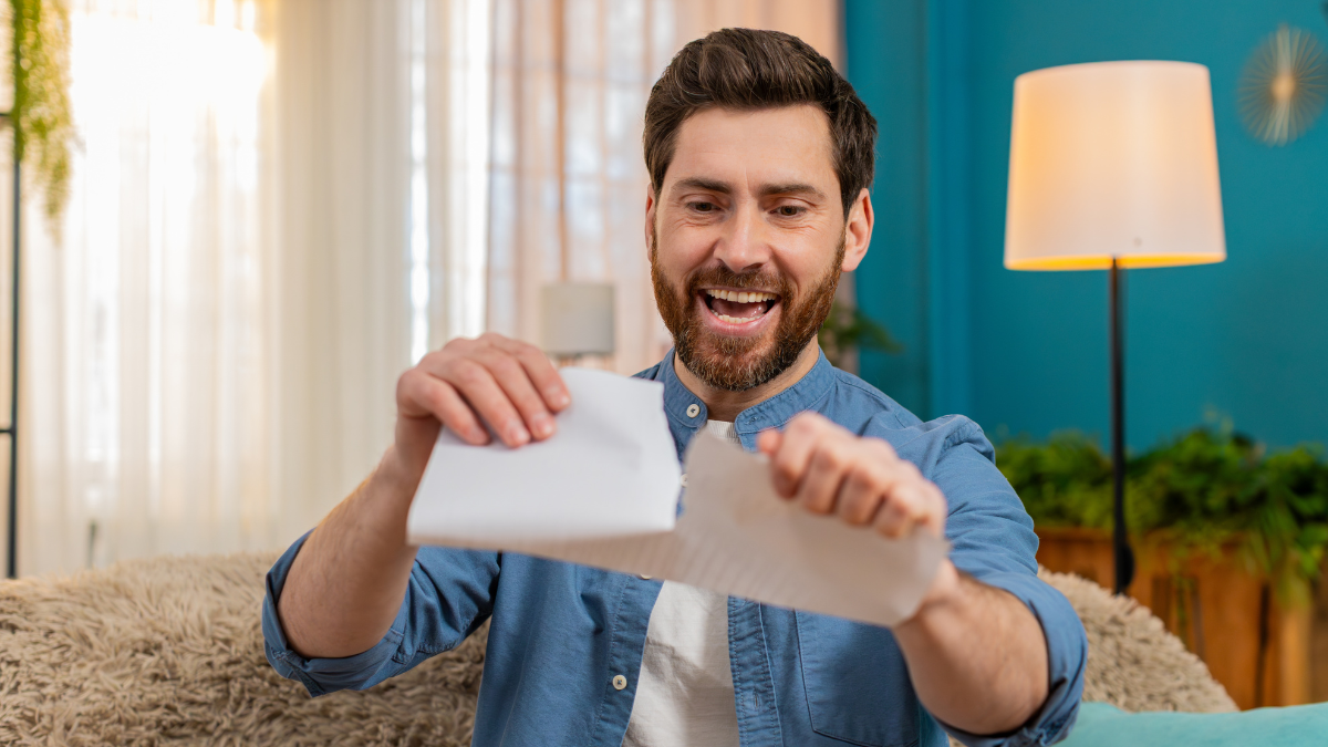 Young man at home sits on the sofa, smiling and tearing an unnecessary document into pieces with relief. Caucasian guy feels happy and free, no longer worried about obligations, debts, or past issues debt snowball,